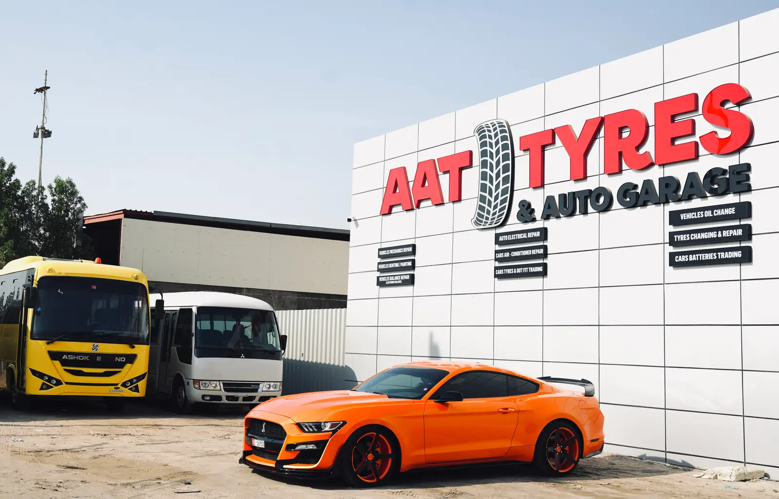 The AAT Tyres & Auto Garage building, its name on the facade, with two buses and a car parked outside.