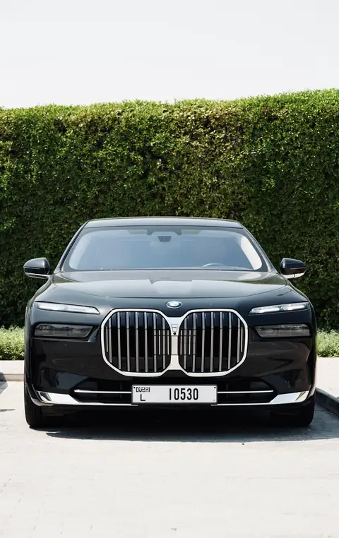 A black BMW 7 Series head-on in front of a hedge