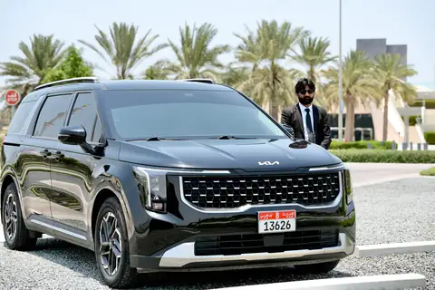 A black Kia Carnival with a chauffeur beside it