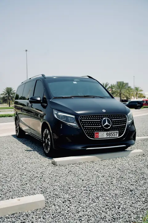 A black Mercedes-Benz V-Class head-on, parked on a gravel verge