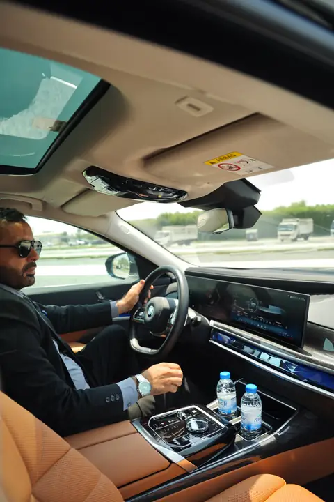 A chauffeur at the wheel of a BMW 7 Series with a tan leather cabin