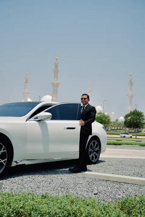 A chauffeur beside a white BMW 7 Series with the Grand Mosque behind