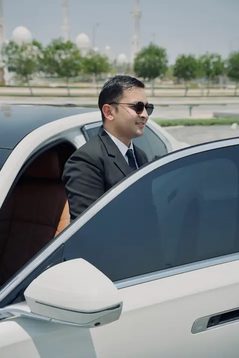 A chauffeur holding open the rear door of a white car