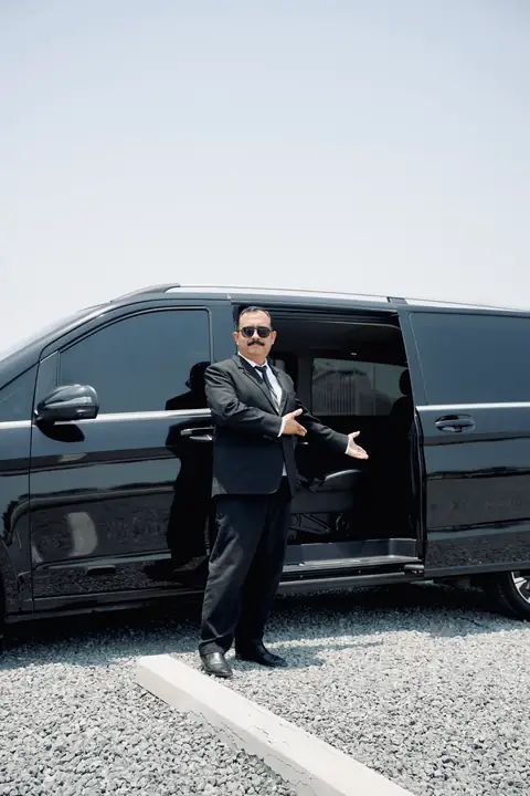A chauffeur holding open the sliding door of a black V-Class