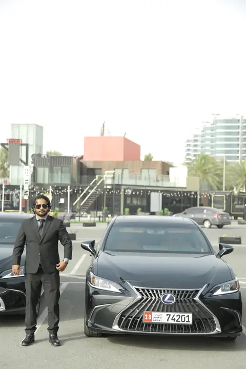 A chauffeur in a dark suit standing beside a black Lexus