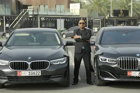A chauffeur in a dark suit standing between two black BMW sedans