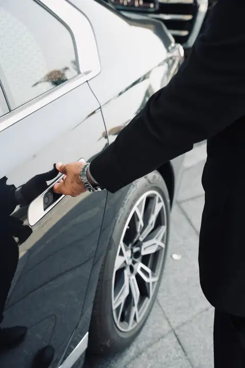 A chauffeur's hand on a car door handle