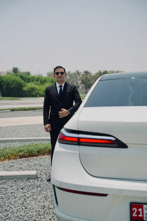 A chauffeur standing behind a white BMW 7 Series