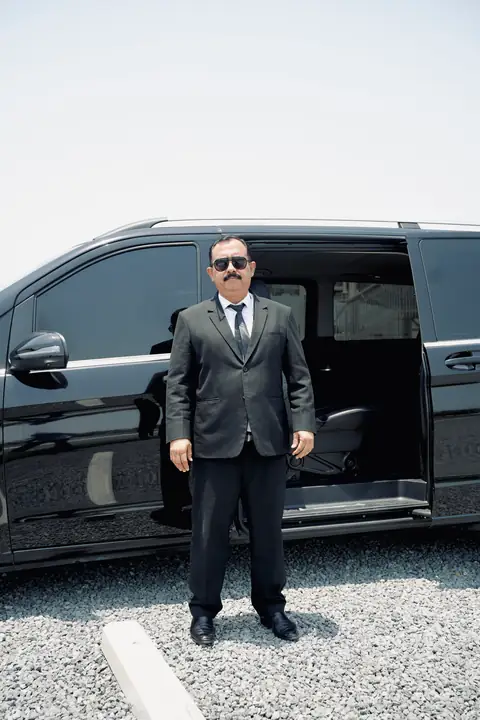 A chauffeur standing beside the open door of a black V-Class