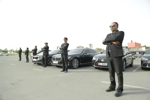 A chauffeur with folded arms in front of a row of black cars