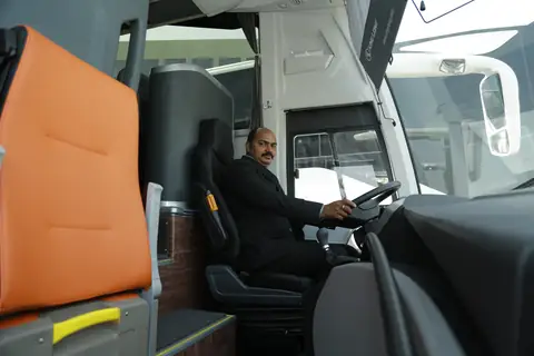 A coach driver in a dark jacket at the wheel, seen through the open door