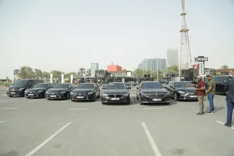 A line of black sedans and an SUV, chauffeurs standing at the far end