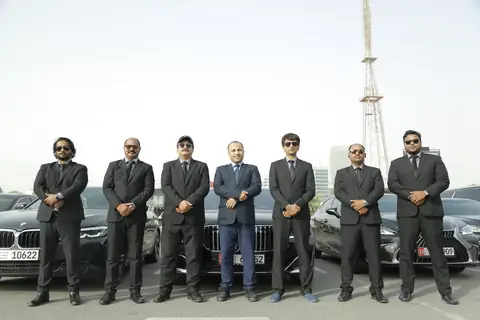 A line of chauffeurs in dark suits in front of black cars