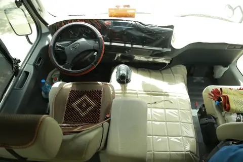 A minibus driving seat with a beaded cover and a wood-trim wheel