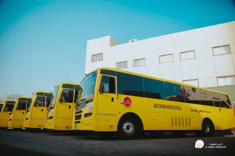 A row of yellow school buses parked outside a school building under a clear sky