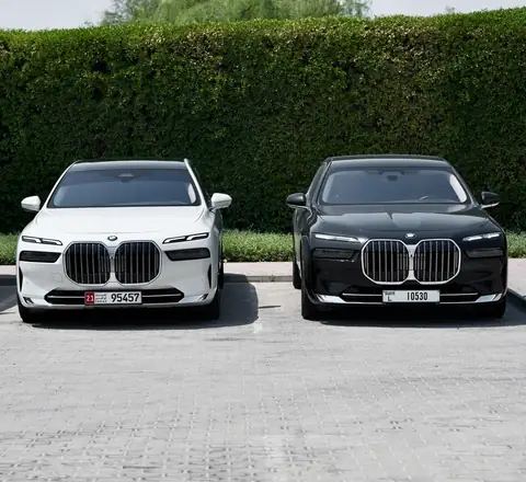 A white and a black BMW 7 Series parked in front of a hedge