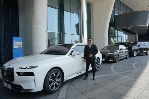 A white BMW 7 Series and a chauffeur at a building's entrance