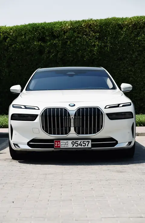 A white BMW 7 Series head-on in front of a hedge