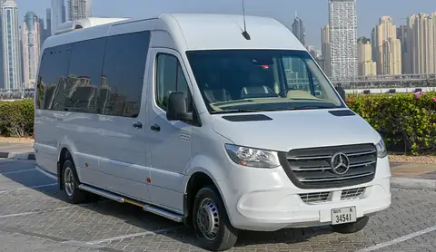 A white Mercedes-Benz Sprinter van on Dubai plates with a skyline of tall towers behind
