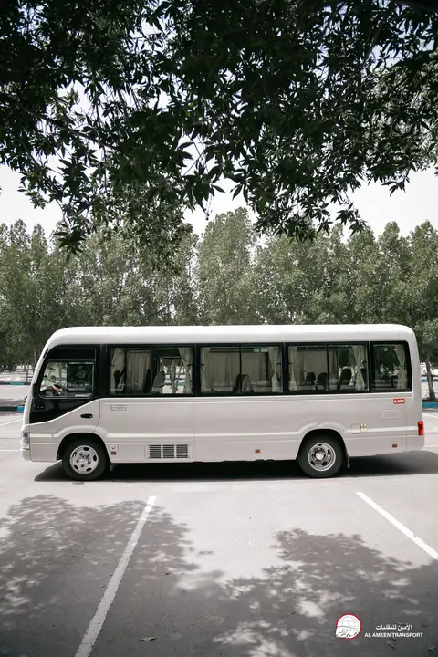 A white minibus in a tree-lined car park, seen from a distance