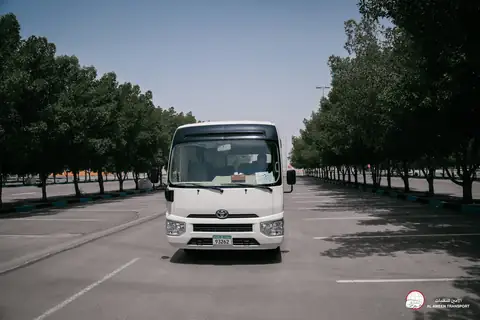A white Toyota minibus head-on in a tree-lined car park