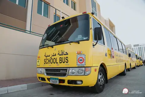 A yellow school minibus with School Bus on its windscreen, parked in a line