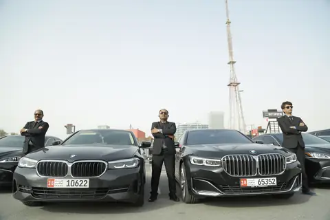 Chauffeurs in dark suits, arms folded, beside black cars