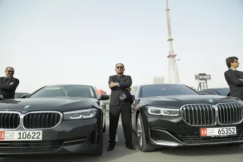 Four chauffeurs standing by two black BMW sedans