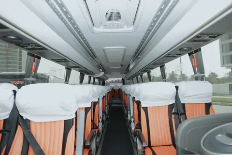 Inside a coach: rows of seats with white headrest covers and orange trim