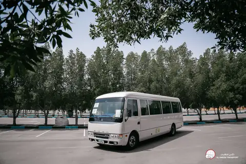 Side view of a white minibus in a tree-lined car park