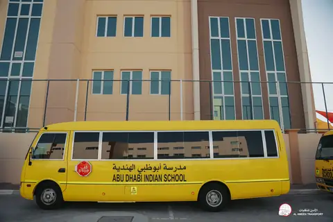 Side view of a yellow school minibus lettered Abu Dhabi Indian School, the school wall behind