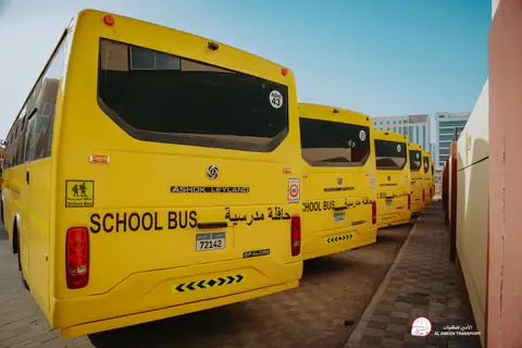 The rear of a yellow school bus with School Bus lettering and hazard stripes, more buses behind