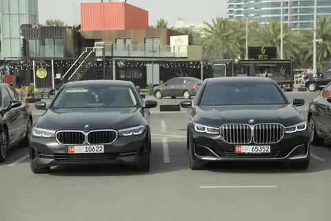 Two black BMW sedans head-on with buildings behind