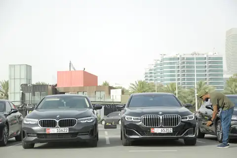 Two black BMW sedans with chauffeurs beside them