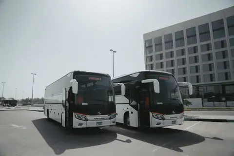 Two white coaches parked side by side with a tower block behind