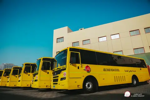 Yellow school buses parked in a line beside a school building
