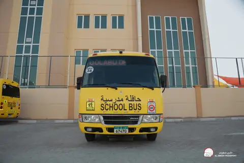 Yellow school minibuses in a line, the school's tall windows behind